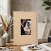 A light beige linen photo album with a framed picture of a couple on a wooden table.