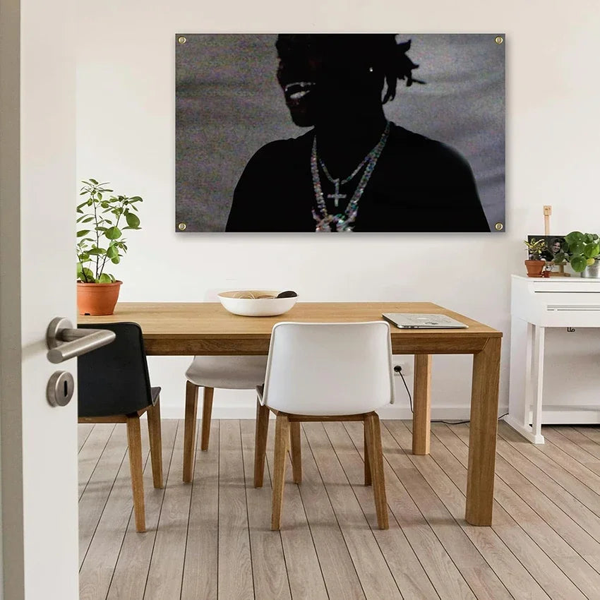 A dark portrait of a person wearing a necklace is displayed on a canvas above a wooden dining table.