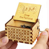 A carved wooden music box with a lid featuring musical notes and the text Over the Rainbow is held in a hand.
