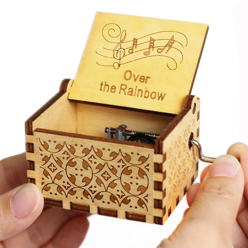 A carved wooden music box with a lid featuring musical notes and the text Over the Rainbow is held in a hand.