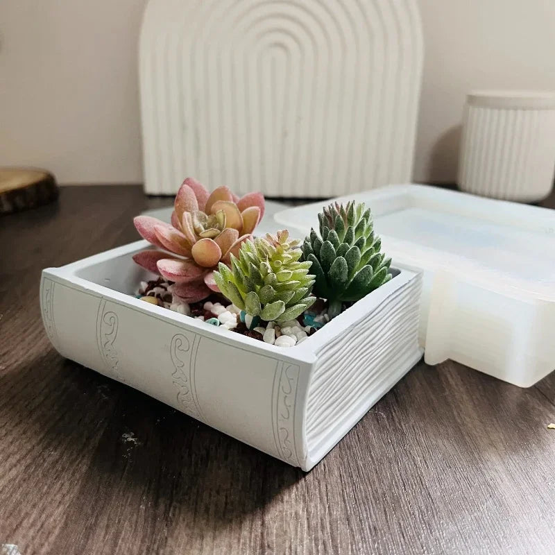 A white book-shaped silicone mold containing succulents for resin and concrete DIY projects.