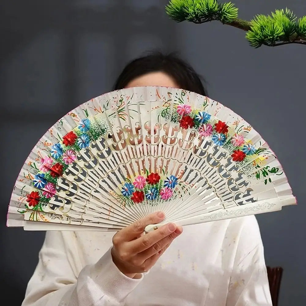 A person holds an open hand-painted decorative folding fan with floral designs against a dark background.