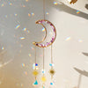A handcrafted moon crystal suncatcher featuring a gold crescent and purple crystals with dangling prism beads.