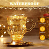 A glass mug filled with glowing copper wire fairy lights on a saucer, demonstrating waterproof and flexible features.