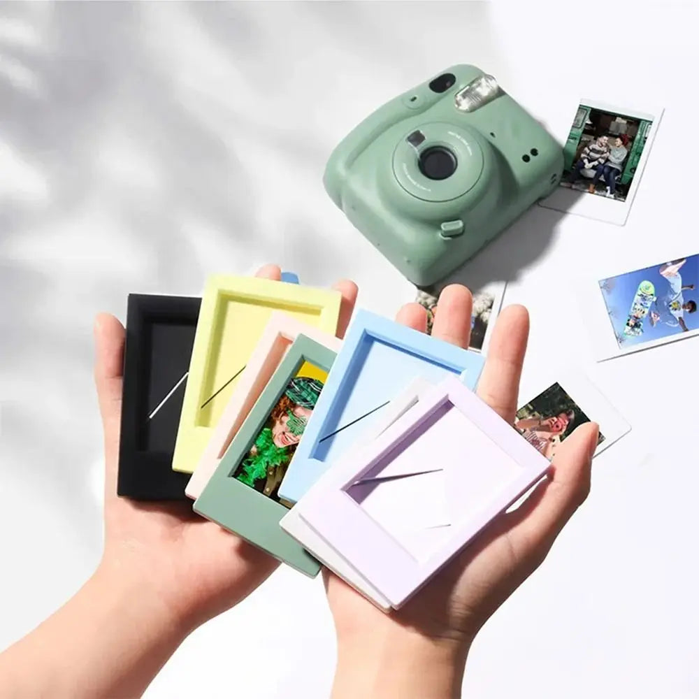 A hand holds a green mini film frame displaying instant photos, next to a vintage camera.