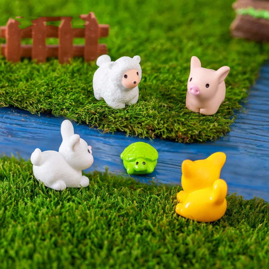A set of mini white and pink pig and lamb figurines placed in a green artificial grass garden setting.