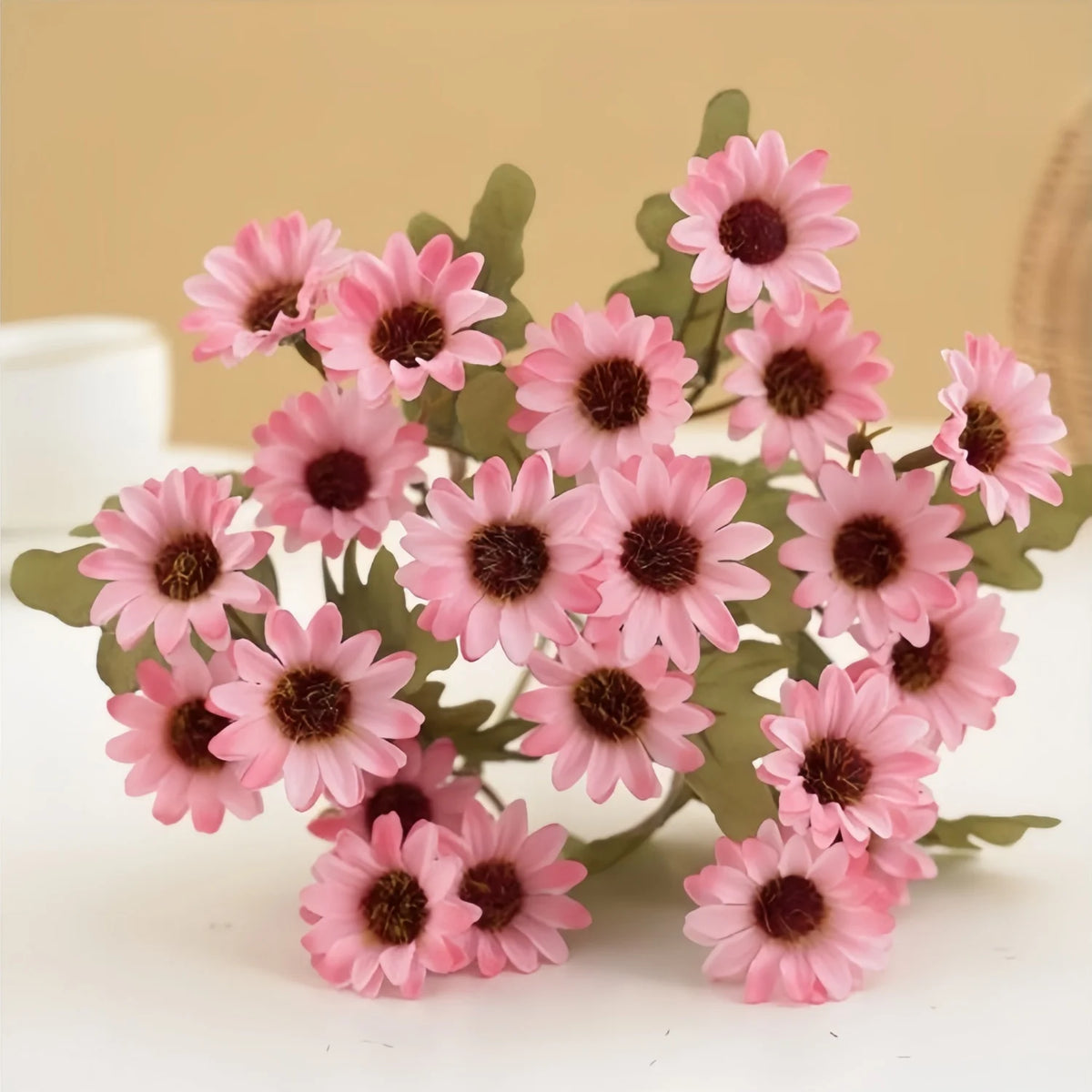 A cluster of three pink silk gerbera daisy artificial flowers on a white surface.