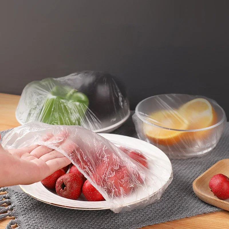 A hand is holding a piece of reusable clear cling film over fresh red strawberries on a white plate.