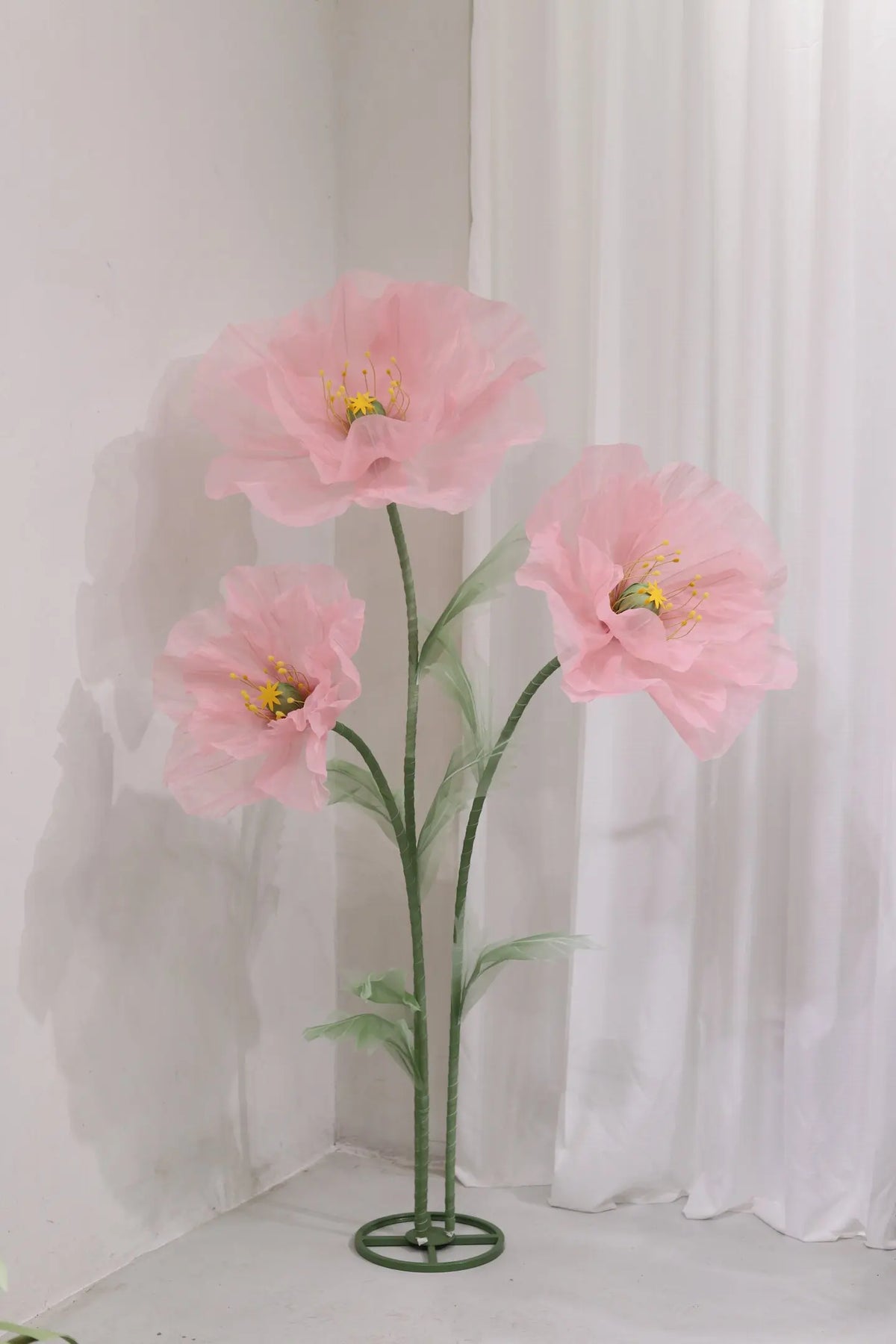 A large artificial silk pink poppy flower arrangement displayed on a green stand against a white background.