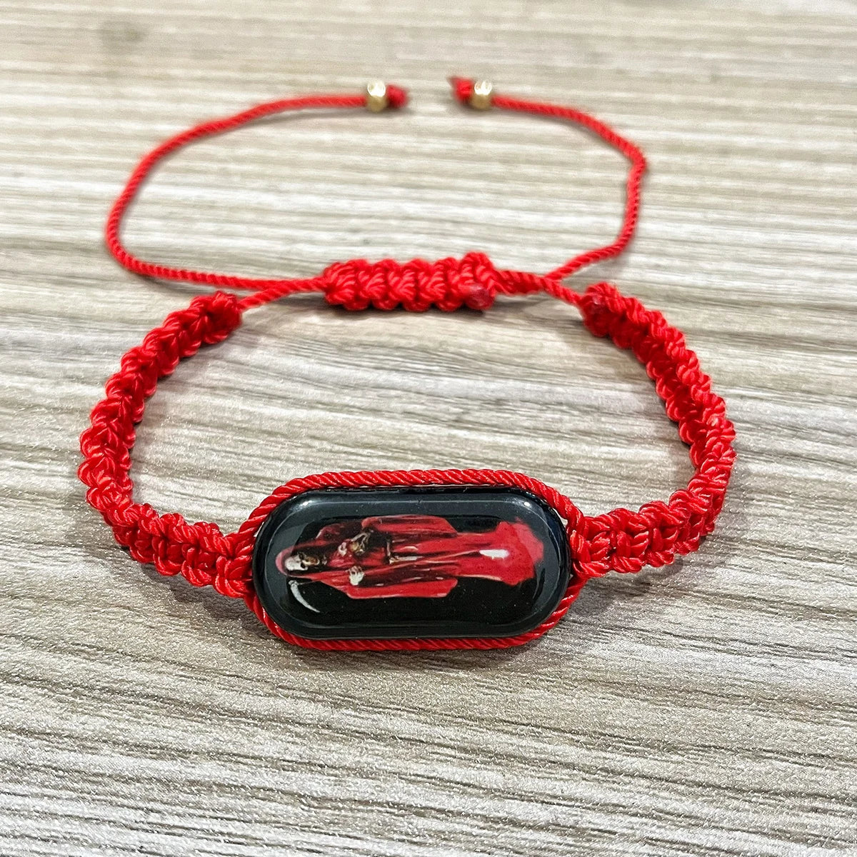A red woven bracelet featuring a black oval charm depicting a religious figure.