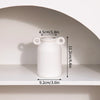A white ceramic vase with a round body and two handles is displayed on a shelf.