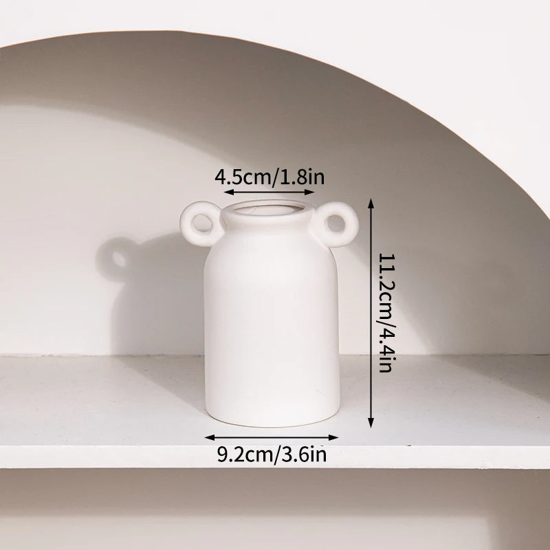 A white ceramic vase with a round body and two handles is displayed on a shelf.