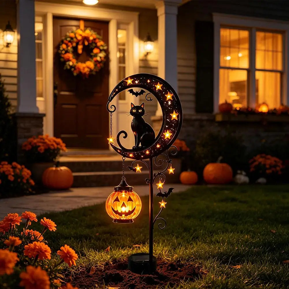 A decorative stake light featuring a black cat silhouette and pumpkin moon design in an outdoor garden setting.