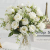 A bouquet of white silk touch artificial roses and greenery displayed in a glass vase.