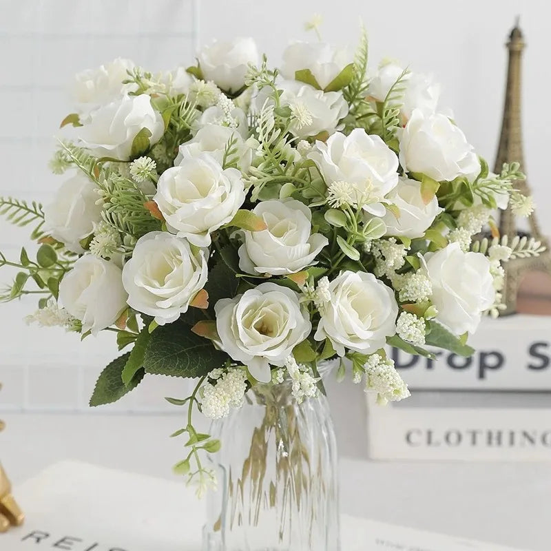 A bouquet of white silk touch artificial roses and greenery displayed in a glass vase.