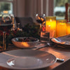 A close-up of a dinner setting featuring two glowing yellow tea light candles on a wooden table.