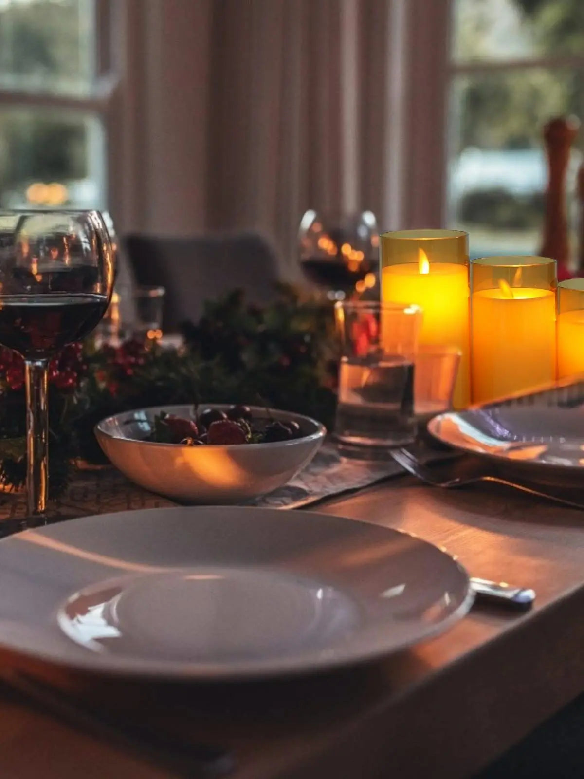 A close-up of a dinner setting featuring two glowing yellow tea light candles on a wooden table.