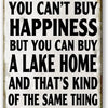 A distressed metal sign with black text that reads You can't buy happiness but you can buy a lake home and that's kind of the