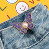 A purple and gold butterfly clip attached to a denim jean pocket.