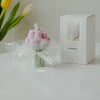 A pink tulip bouquet in a glass vase next to its retail box for a healing life soy wax candle