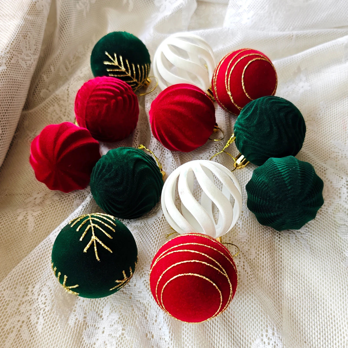 A collection of 30 velvet Christmas baubles in red, green, and white, decorated with gold leaf, displayed on a white fabric.