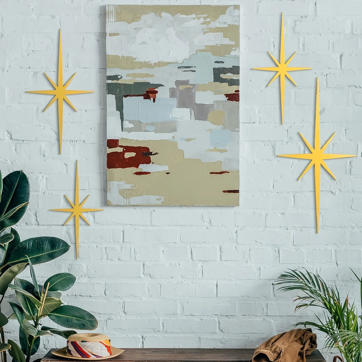 A modern metal star wall art set featuring four gold-colored stars mounted on a white brick wall above an abstract landscape 