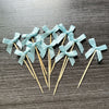 A set of light blue ribbon bows on wooden sticks used as cupcake toppers.