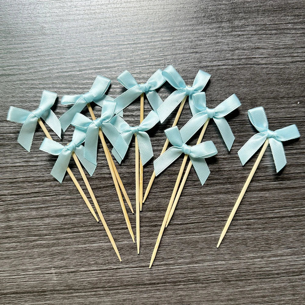 A set of light blue ribbon bows on wooden sticks used as cupcake toppers.