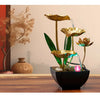 A golden tabletop fountain featuring green leaves and water spouts on a dark bowl.