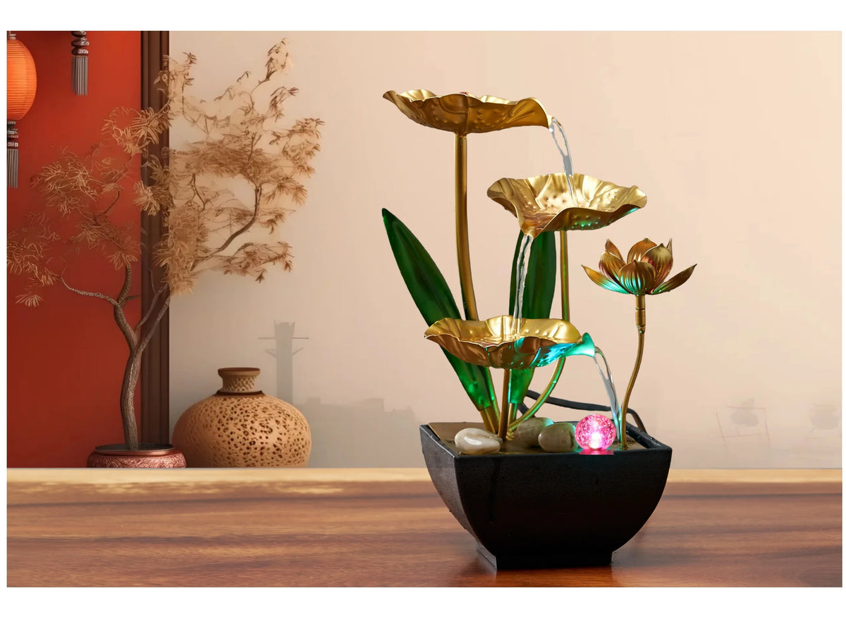 A golden tabletop fountain featuring green leaves and water spouts on a dark bowl.