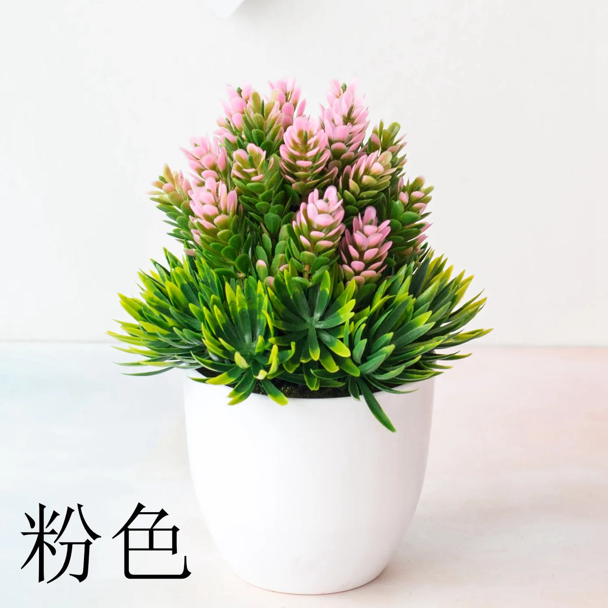 Un pot de bonsaï artificiel avec du feuillage rose et vert sur une surface blanche.