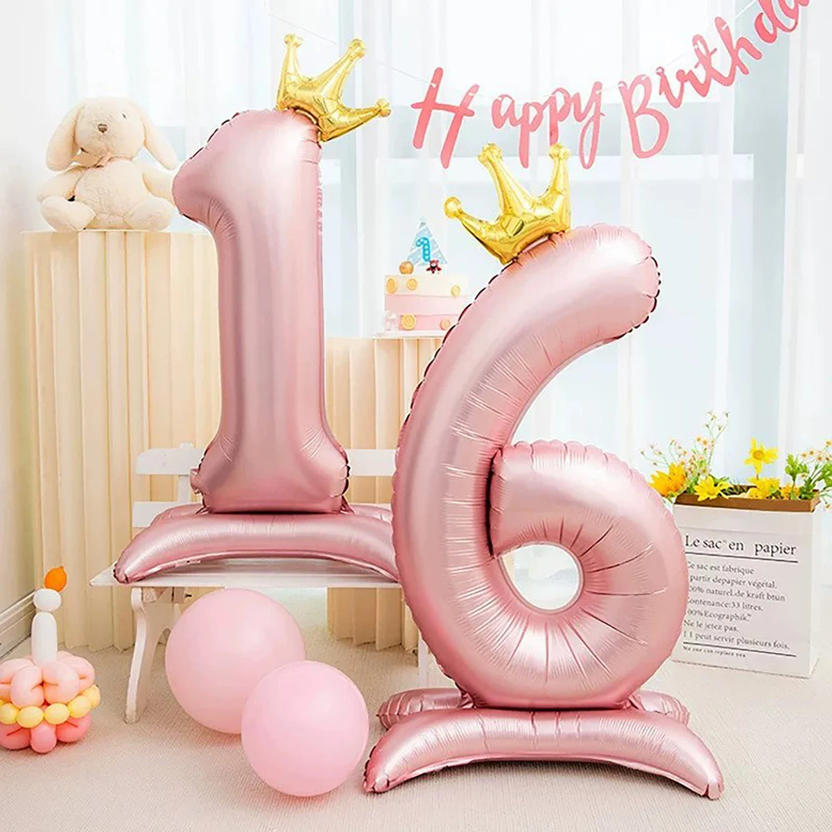 A large pink foil balloon shaped like the number one stands next to a gold crown and other balloons for a birthday celebratio