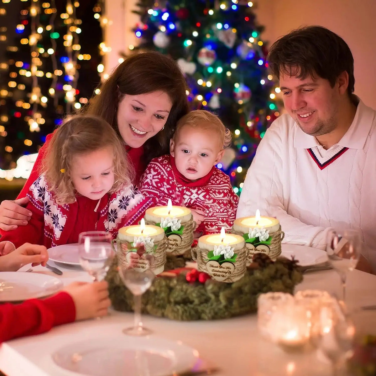 A family is gathered around a table with glowing tealight candle holders in a festive setting.