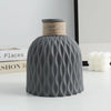 A gray plastic vase with a textured, ripple pattern and a woven straw lid, displayed on a white surface.