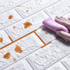 A hand is applying a pink exfoliating mitt onto white foam brick wallpaper panels that have orange stains on them.