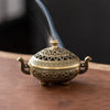 A vintage brass incense burner holder with a lid and handles, emitting smoke.