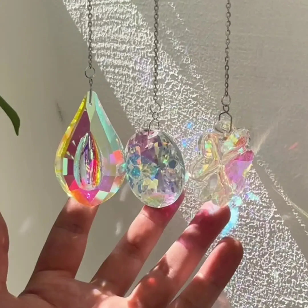 A hand holds three hanging crystal wind chimes or suncatchers with iridescent facets.