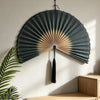 A handwoven bamboo wall fan decor with a dark gray and beige striped design mounted on a white wall.