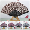 A leopard print folding hand fan with a black handle displayed on a wooden stand.
