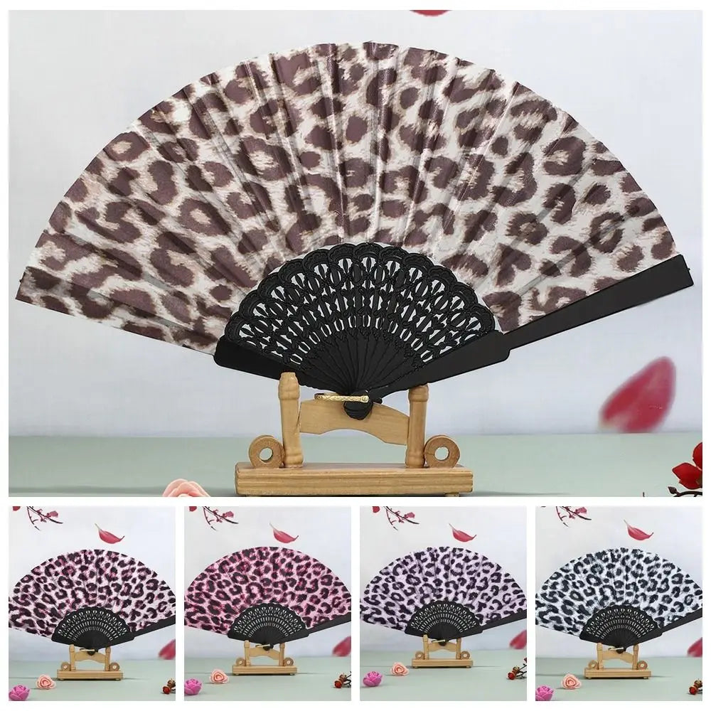 A leopard print folding hand fan with a black handle displayed on a wooden stand.