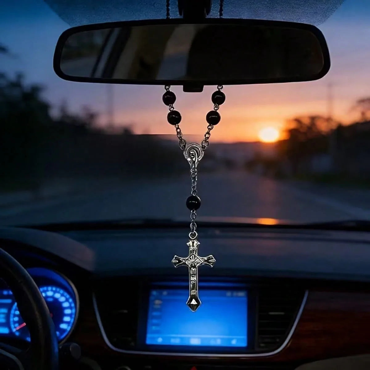 A silver cross pendant and chain are hanging from a rearview mirror inside a car.