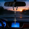A silver cross pendant and chain are hanging from a rearview mirror inside a car.
