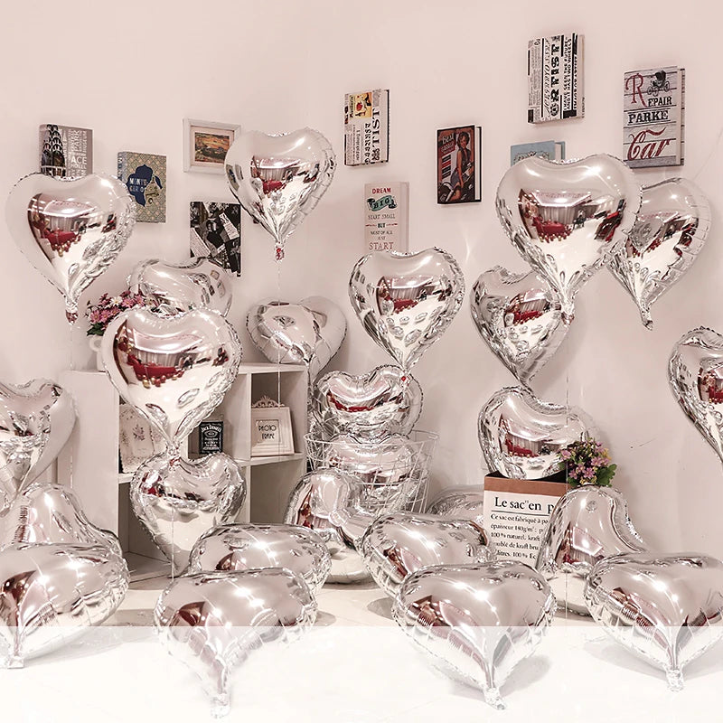 A display of silver heart foil balloons arranged on a white wall and table.