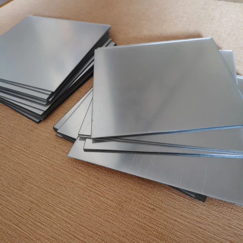 A stack of four silver self-adhesive acrylic mirror wall stickers placed on a brown surface.