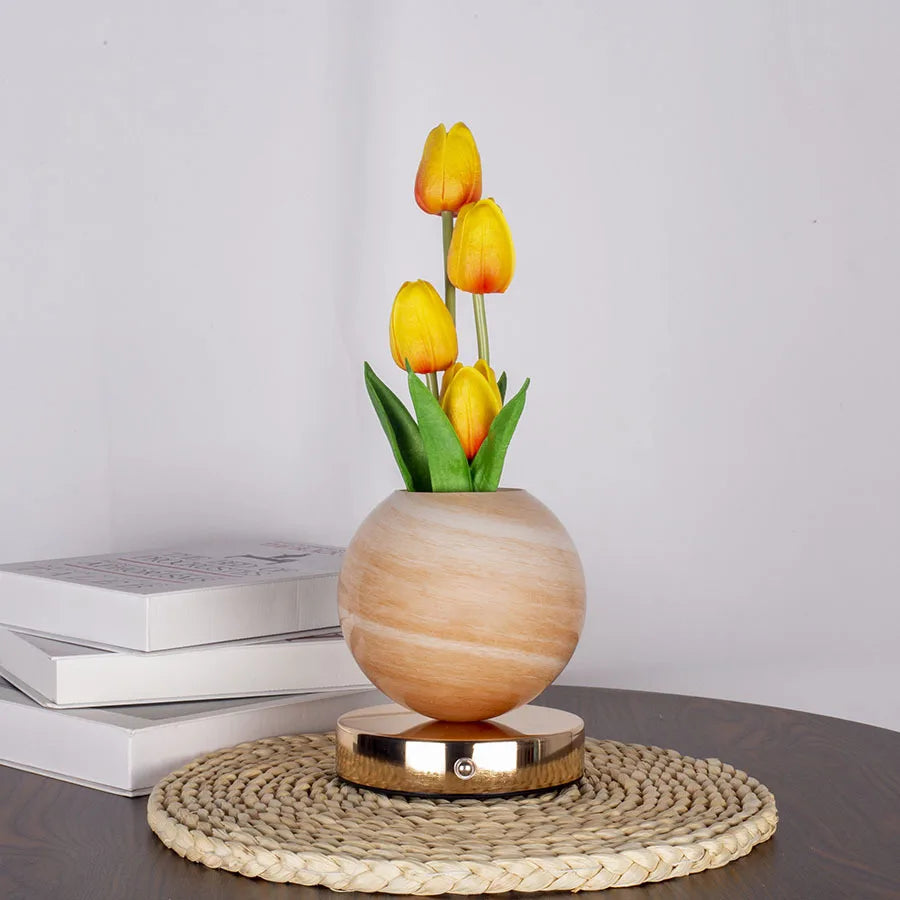 A vase holds three yellow tulips, set on a woven mat and resting on a dark surface.