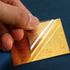A hand holds a gold-colored sticker for prosperity and good fortune against a dark blue background.
