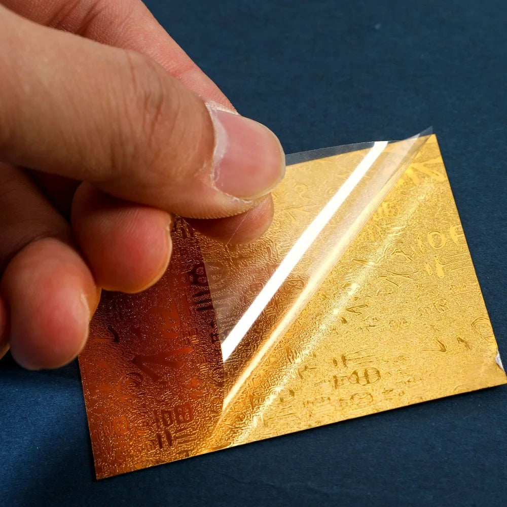 A hand holds a gold-colored sticker for prosperity and good fortune against a dark blue background.
