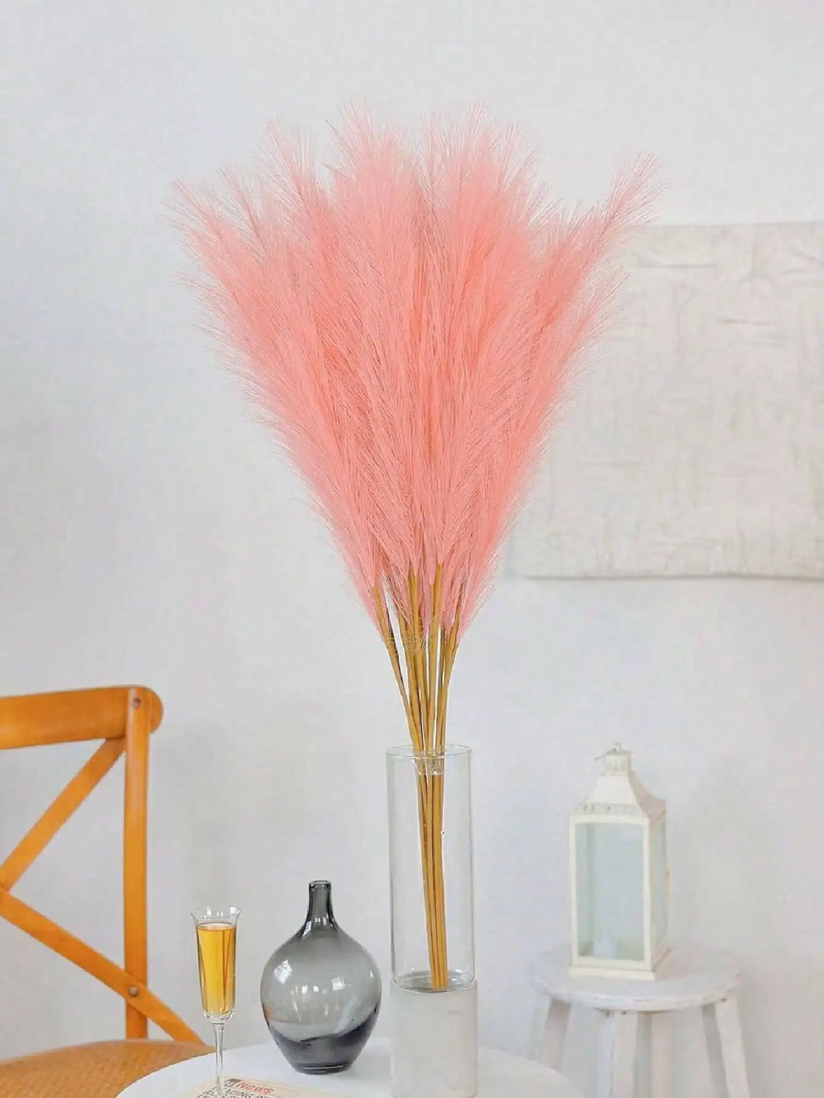 A bouquet of pink pampas grass stems in a glass vase displayed on a white surface.