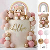 A white cake decorated with pink and gold ball decorations and a teddy bear topper, surrounded by rainbow-colored balloons.