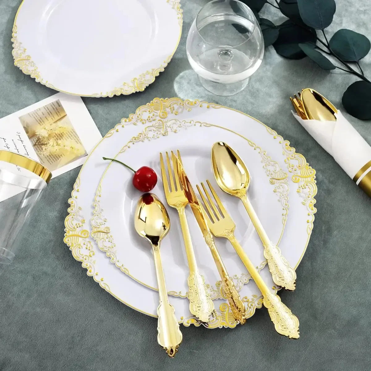 Elegant white and gold disposable dinnerware set with cutlery arranged on a gray surface.